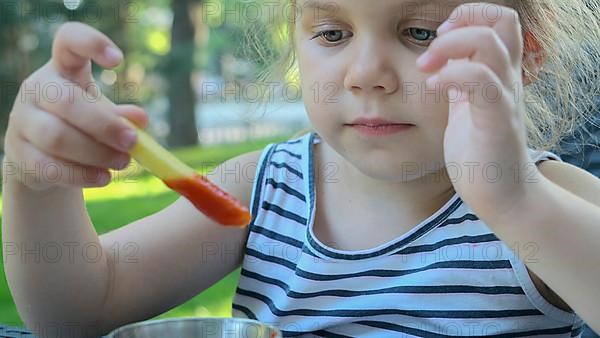 Little girl eat french fries. Close-up of blonde girl takes potato chips with her hands and tries them sitting in street cafe on the park. Odessa Ukraine