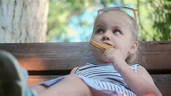 Little girl eats gingerbread. Close-up portrait of blonde girl sitting on park bench and eating cookies. Odessa Ukraine