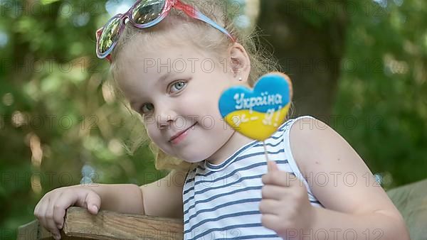 Little blonde girl holds gingerbread in Ukrainian national colors in her hand