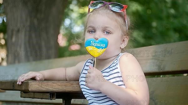 Little blonde girl holds gingerbread in Ukrainian national colors in her hand