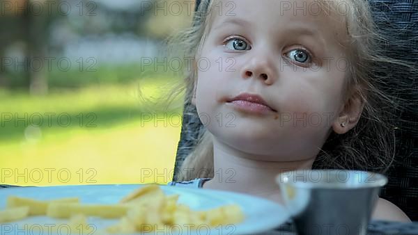 Little girl eat french fries. Close-up of blonde girl takes potato chips with her hands and tries them sitting in street cafe on the park. Odessa Ukraine