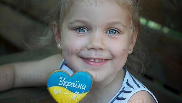 Little blonde girl holds gingerbread in Ukrainian national colors in her hand