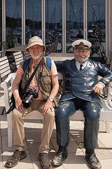 Elderly gentleman sitting next to captain figure