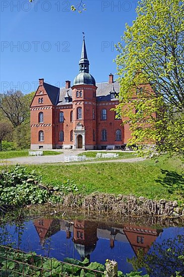 Red manor house reflected in a ditch