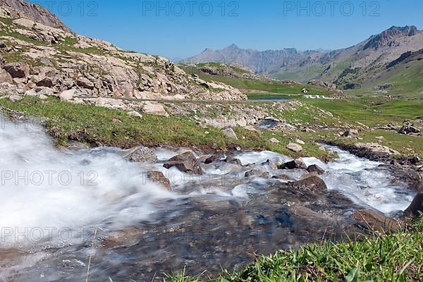 View of torrential mountain stream tributary of Lac des Eissaupres in the background next to mountain road of Route de Col de la Bonette e Restefond