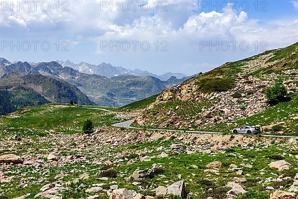 Porsche GT3 sports car drives on 2350 metre high Passo Lombarda pass above tree line at French-Italian border