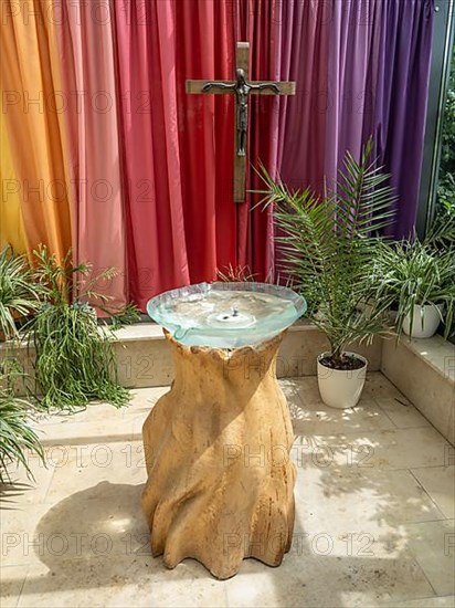 Glass baptismal fountain on a base of ash wood and crucifix in the entrance area of Germany's first private ecumenical motorway church Geiselwind 'Light on our way' on the A 3 between Wuerzburg and Nuremberg