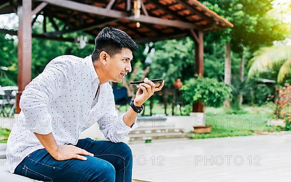 Handsome man sitting outside sending a voice message with his cell phone
