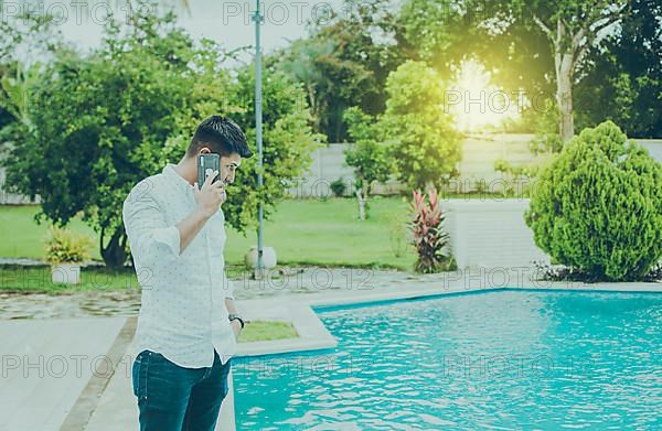 Handsome man calling on the phone by a swimming pool