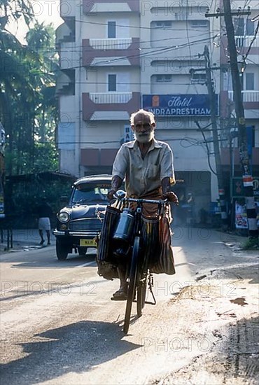 An old man riding bicycle with luggage on the handlebars in Kodungallur