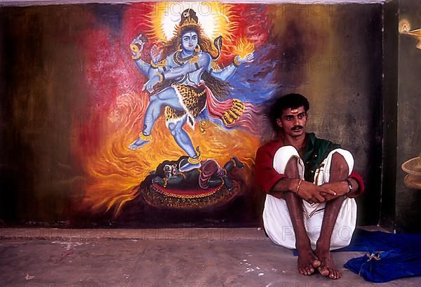 A man sitting near the mural of Lord shiva in Wadakancherry Siva Temple