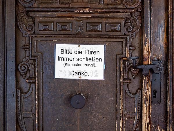 Portal of the Catholic parish church of St. George with sign 'Please always close the bags