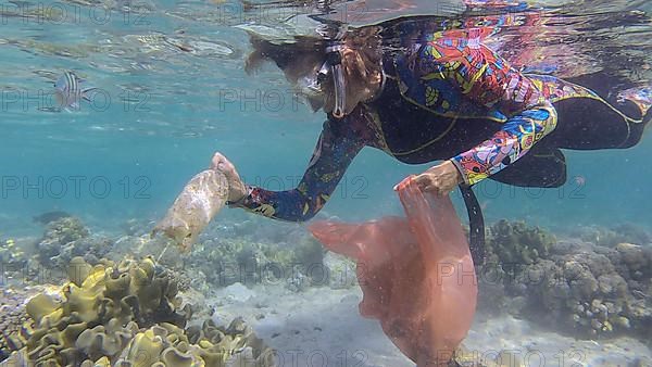 Woman in diving equipment swims and collects plastic debris underwater on the bottom of coral reef. Snorkeler cleaning Ocean from plastic pollution. Plastic pollution of the Ocean. Red sea