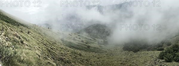 Panoramic view of low-hanging clouds in valley of mountain landscape in Alps