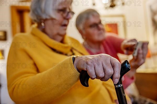 Senior citizen with crutch is shown a smartphone by her sister