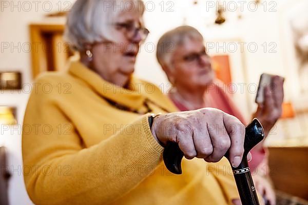 Senior citizen with crutch is shown a smartphone by her sister