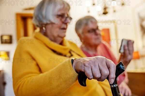 Senior citizen with crutch is shown a smartphone by her sister