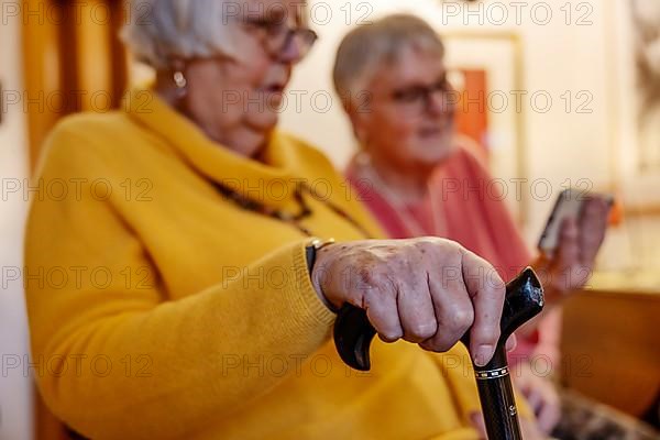 Senior citizen with crutch is shown a smartphone by her sister