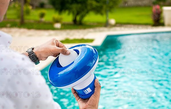 Pool float and chlorine tablets for pool maintenance. Hands holding a pool chlorine dispenser. Hand of a pool disinfection worker holding a dispenser with a chlorine tablet. Hands holding a dispenser with pool chlorine tablet