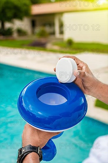 Hand of a pool disinfection worker holding a dispenser with a chlorine tablet. Hands holding a dispenser with pool chlorine tablet