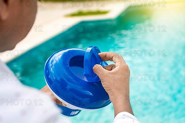 Hand of a pool disinfection worker holding a chlorine dispenser. Hands of a worker installing a pool chlorine float