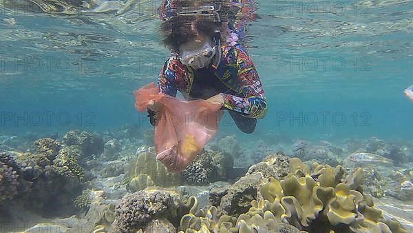 Woman in diving equipment swims and collects plastic debris underwater on the bottom of coral reef. Snorkeler cleaning Ocean from plastic pollution. Plastic pollution of the Ocean. Red sea