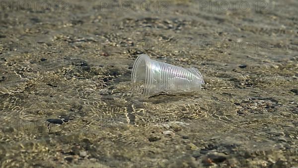 Transparent plastic cup is carried away by the wind to the sea in the coastal zone. Plastic pollution of the surf zone. Red sea