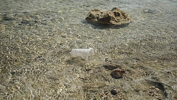 Transparent plastic cup is carried away by the wind to the sea in the coastal zone. Plastic pollution of the surf zone. Red sea