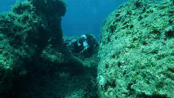 Scuba diver swim through a crack in the rock. Crack in the seabed over tectonic plates. Tiktanic displacement of plates at the bottom of sea. Mediterranean Sea