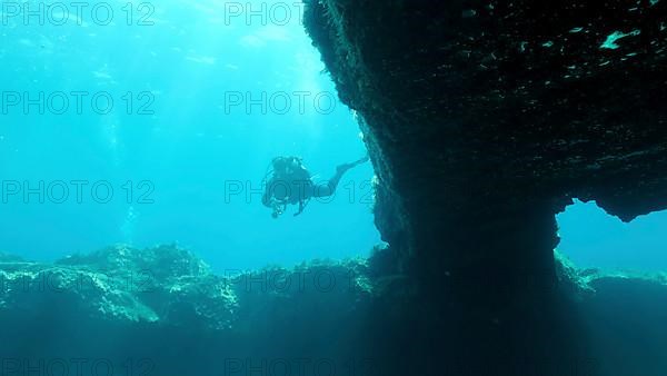 Female scuba diver swim near the exit from the cave. Cave diving in Mediterranean Sea