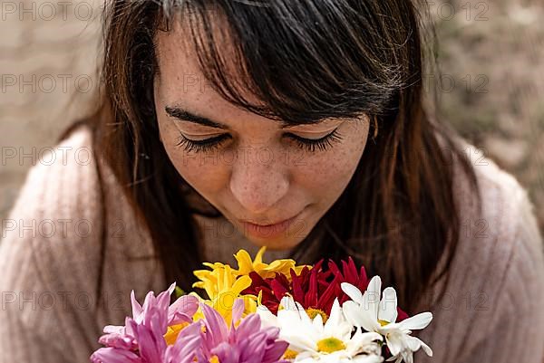 High angle view of a young woman smelling a bouquet of daisies in her hands. Close-up