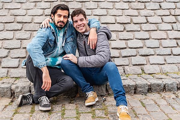 Two male friends hugging and looking at camera outdoors. Copy space