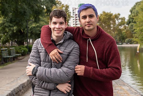 Gay male couple hugging and looking at camera outdoors