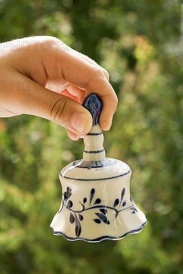 Hand holding a ceramic bell on a green background