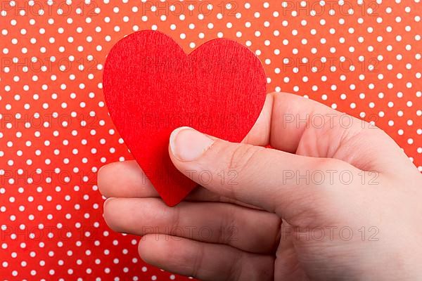 Red color heart shaped object in hand on dotted paper