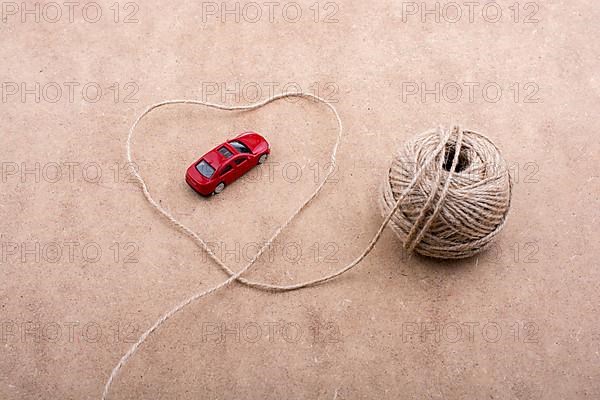 TRed toy car and a spool of thread form a heart shape on background