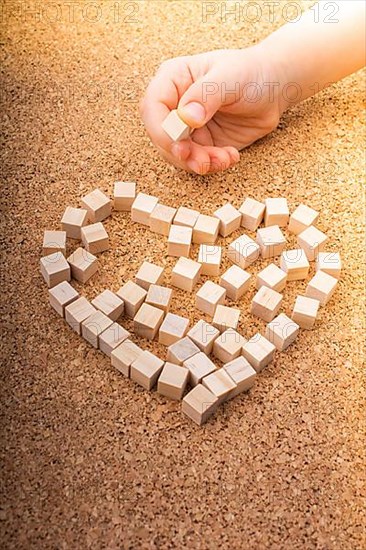 Little wooden cubes form heart shape or valentines day symbol and hand