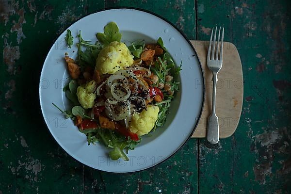 Vegan cauliflower salad on a tin plate with black cumin on a rustic table