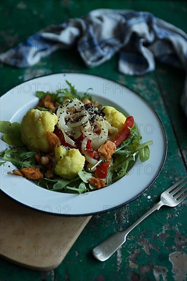 Vegan cauliflower salad on a tin plate with black cumin on a rustic table