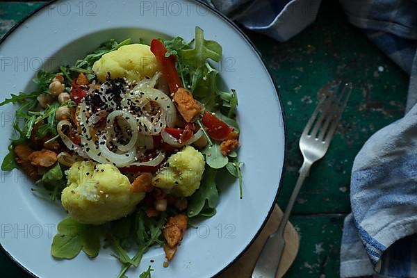 Vegan cauliflower salad on a tin plate with black cumin on a rustic table