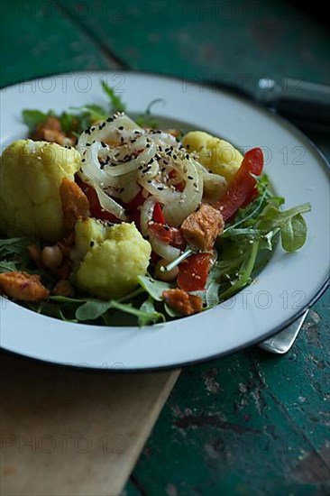 Vegan cauliflower salad on a tin plate with black cumin on a rustic table