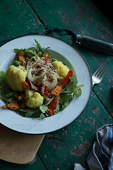 Vegan cauliflower salad on a tin plate with black cumin on a rustic table