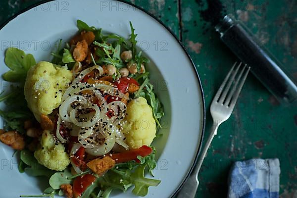 Vegan cauliflower salad on a tin plate with black cumin on a rustic table