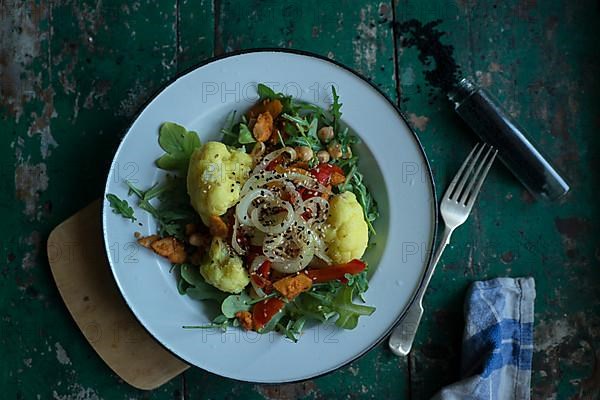 Vegan cauliflower salad on a tin plate with black cumin on a rustic table