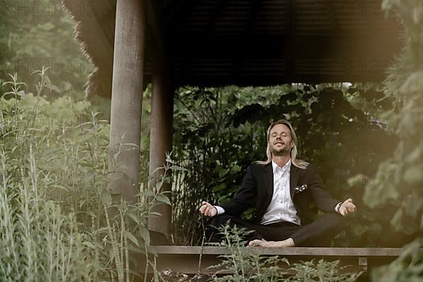 Businessman does yoga on wooden walkway in nature,