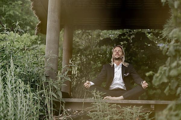 Businessman does yoga on wooden walkway in nature,