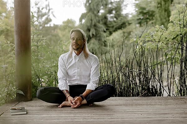 Businessman in white shirt sits on wooden jetty and writes in a book,