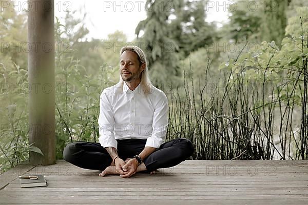 Businessman in white shirt sits on wooden jetty and writes in a book,