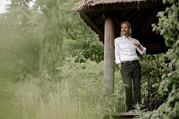 Businessman in a white shirt stands on the wooden jetty in the greenery,