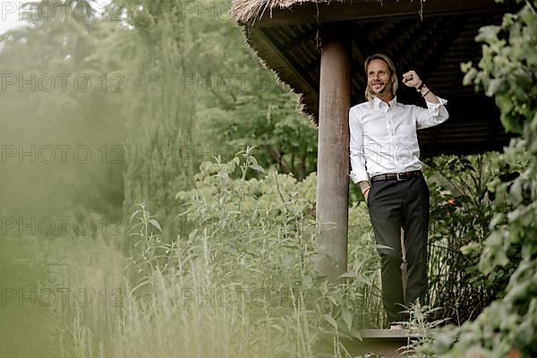 Businessman in a white shirt stands on the wooden jetty in the greenery,